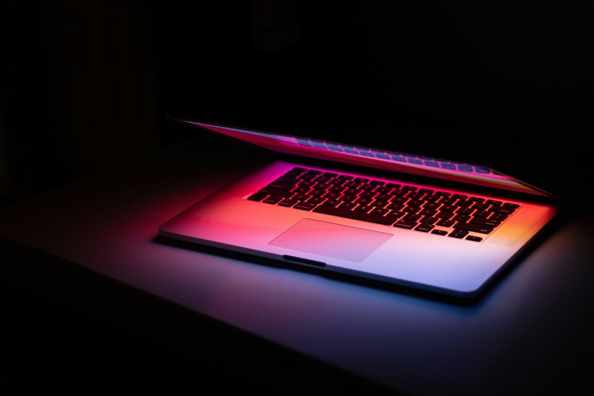 Laptop lit with pink and blue light in a dark environment
